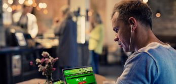 A picture of a man sitting in a bookmakers, checking the odds online on his tablet.