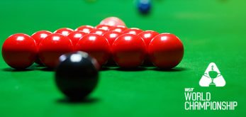 A close-up shot of a snooker table featuring a neatly arranged triangle of red balls and a single black ball positioned in front. The green felt of the table provides a vivid background, while the logo of the WST World Championship is displayed in white text on the right side of the image.