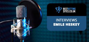 The image shows a professional microphone set up with a pop filter, suggesting a recording or broadcast setting. To the right of the microphone, there's a graphic with the logo of BestBettingSites.co.uk and the text "INTERVIEWS EMILE HESKEY" in a speech bubble format, indicating an interview feature with Emile Heskey, likely related to sports or betting insights.