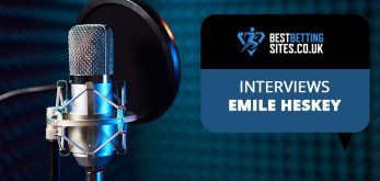 The image shows a professional microphone set up with a pop filter, suggesting a recording or broadcast setting. To the right of the microphone, there's a graphic with the logo of BestBettingSites.co.uk and the text "INTERVIEWS EMILE HESKEY" in a speech bubble format, indicating an interview feature with Emile Heskey, likely related to sports or betting insights.