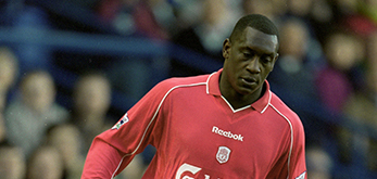The image shows a football player wearing a red Reebok kit, which features the Carlsberg logo and Liverpool FC crest. The player is in action, captured mid-movement during a match, with spectators visible in the background. The setting suggests a lively football game atmosphere.